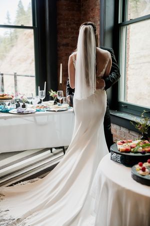 Back view of a wedding dress with flowing train beside elegant table settings and exposed brick walls.