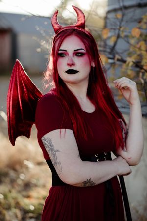 Gothic themed photoshoot with red costume and devil horns in outdoor setting.