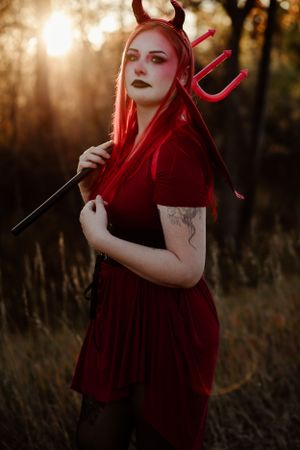 Dramatic outdoor portrait session with devil costume and props at sunset.