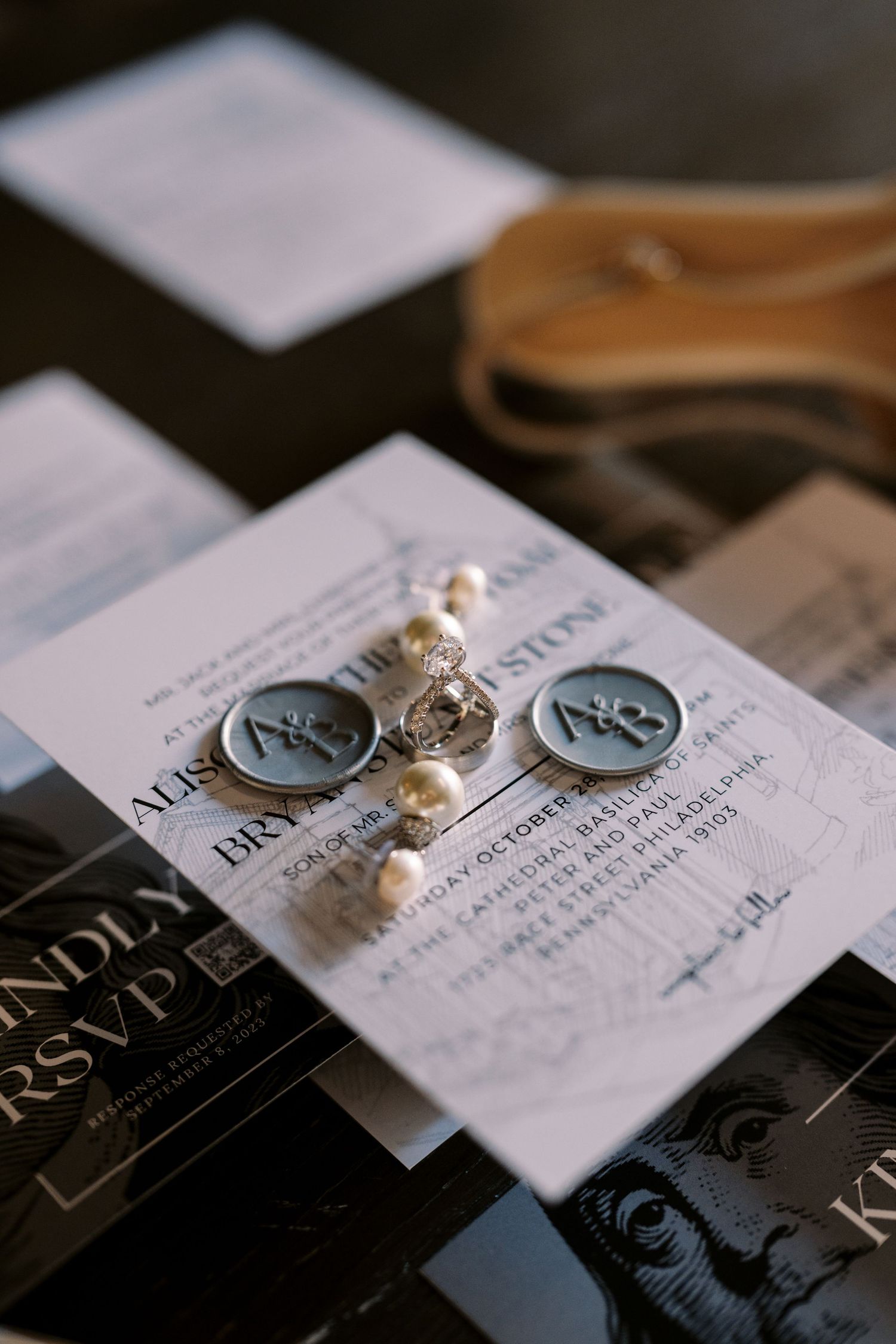 Elegant wedding invitation with pearl details and blue monogram wax seals laid out on dark surface.
