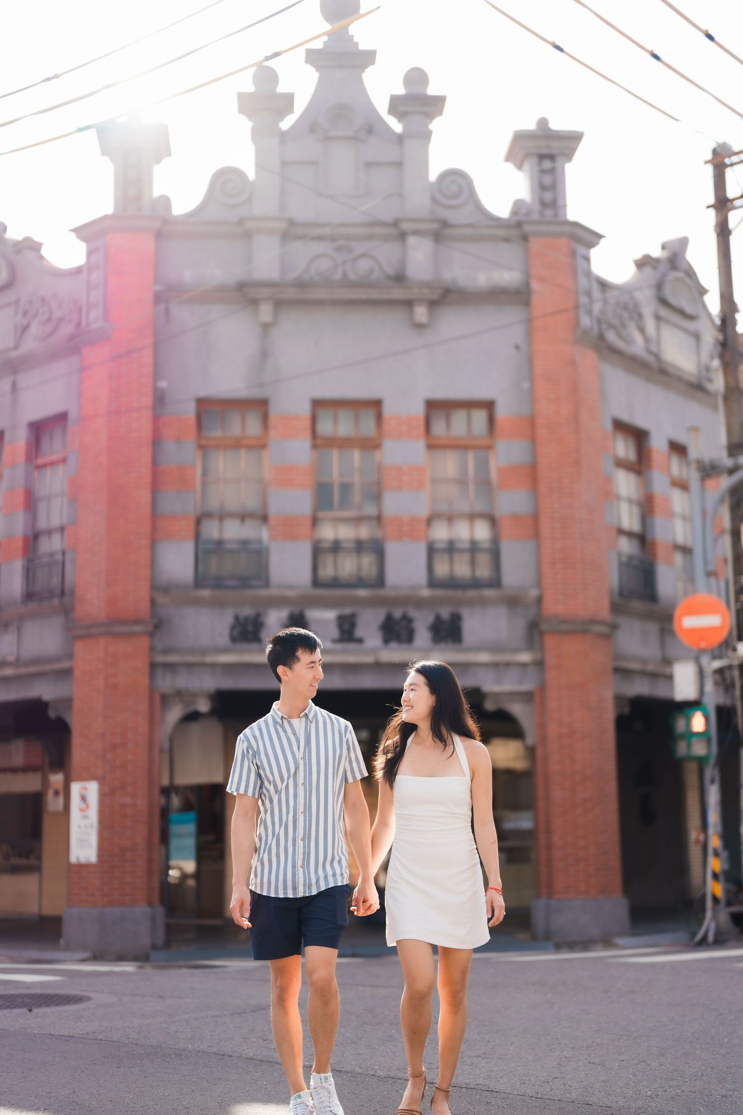 A couple walking hand in hand past a historic building with orange pillars.