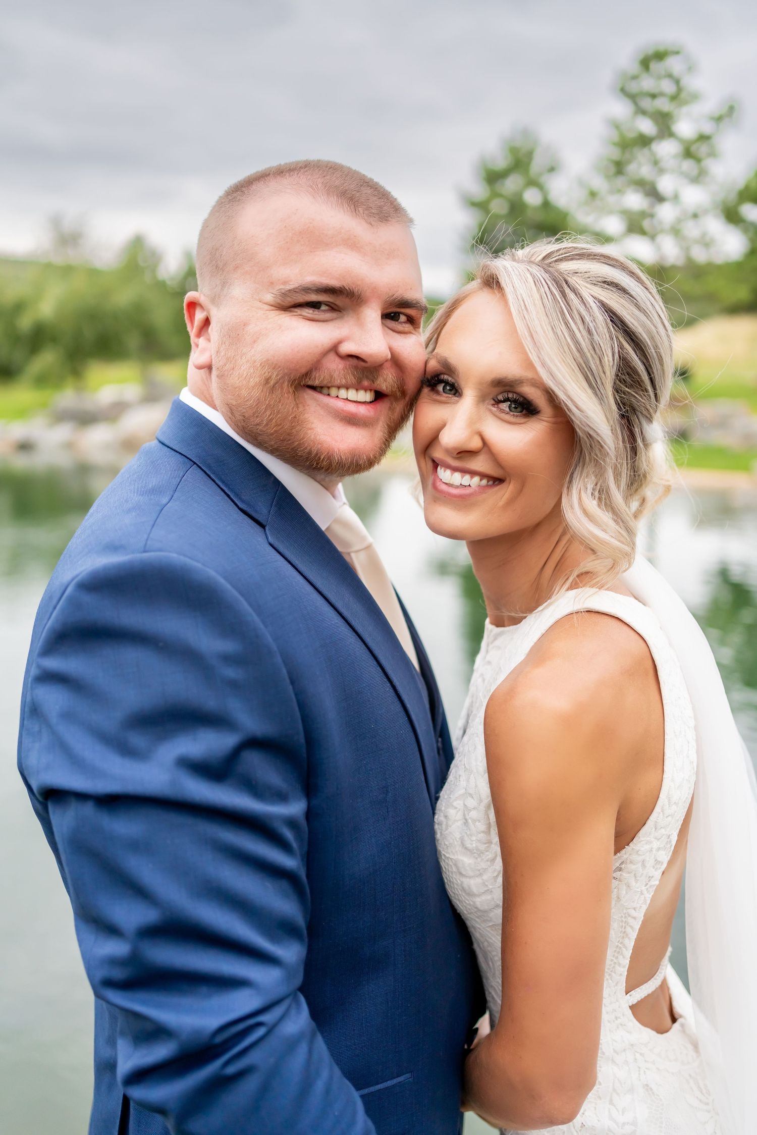Wedding couple smiling together in formal attire against waterfront backdrop.