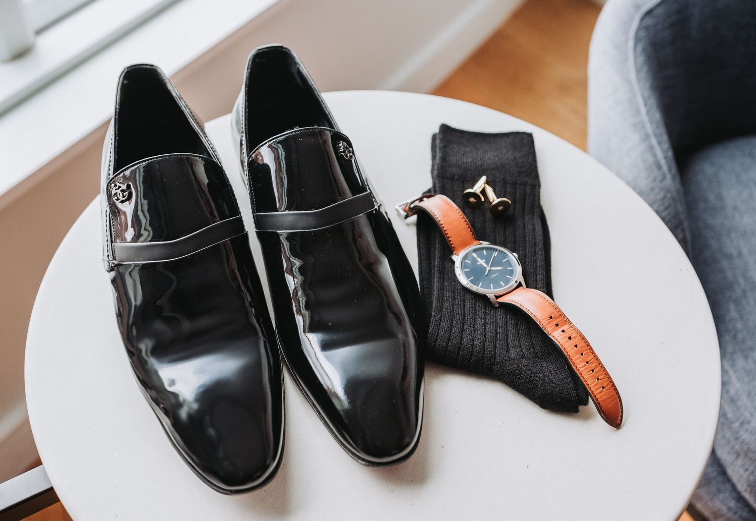 A pair of black patent leather dress shoes with a silver buckle displayed next to a leather watch.  Groom's personal items for wedding.
