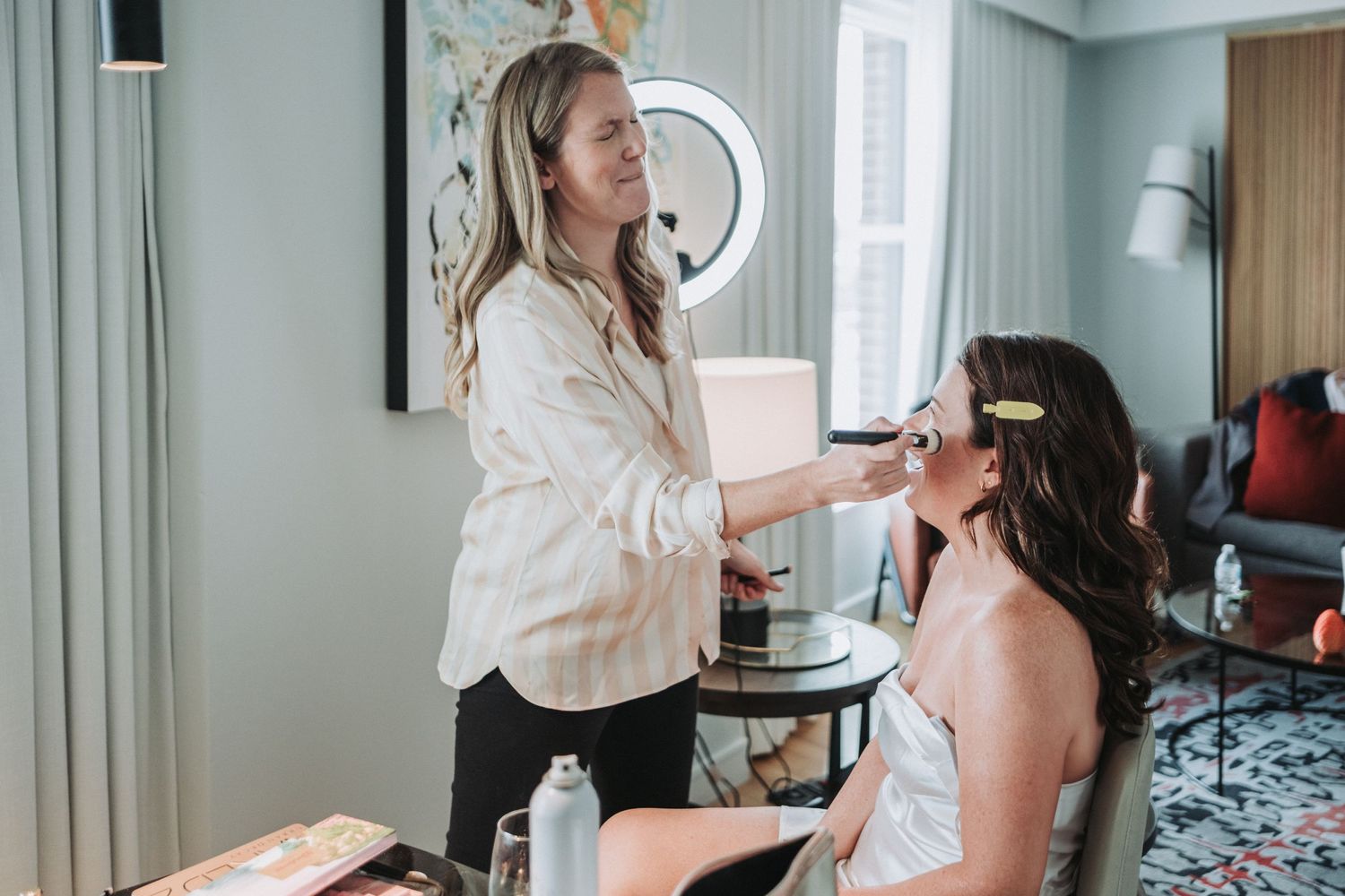 A hair and makeup session takes place in a modern room with teal walls and a patterned area rug.  The bride-to-be is getting ready.