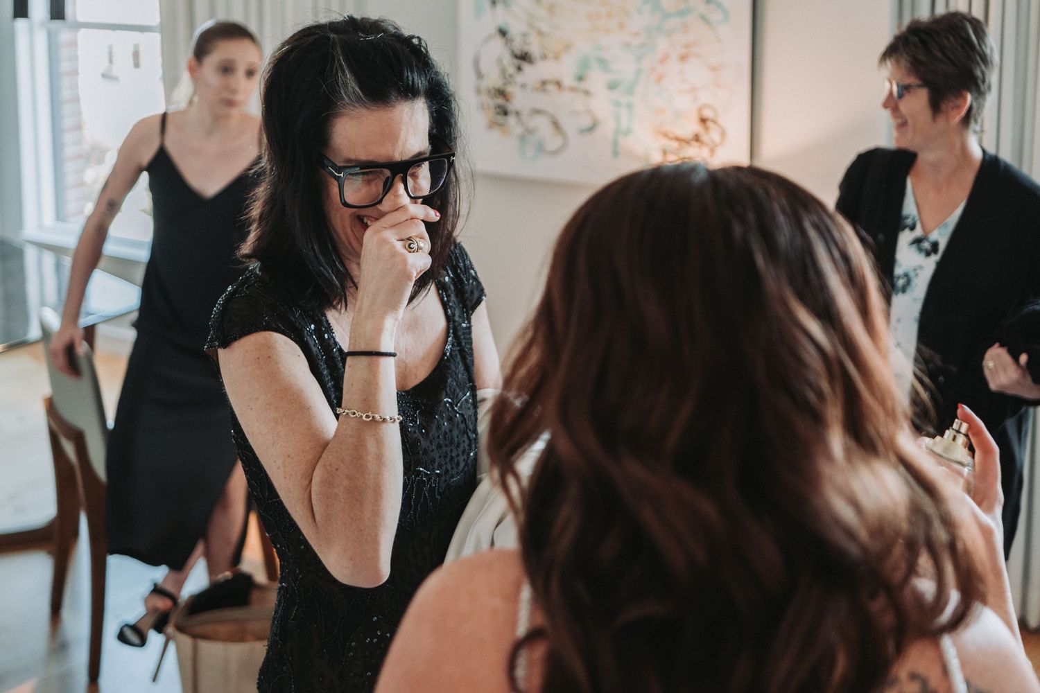 A candid moment at a gathering shows people interacting and conversing in an indoor setting.  A friend sees her BFF ready for her wedding!