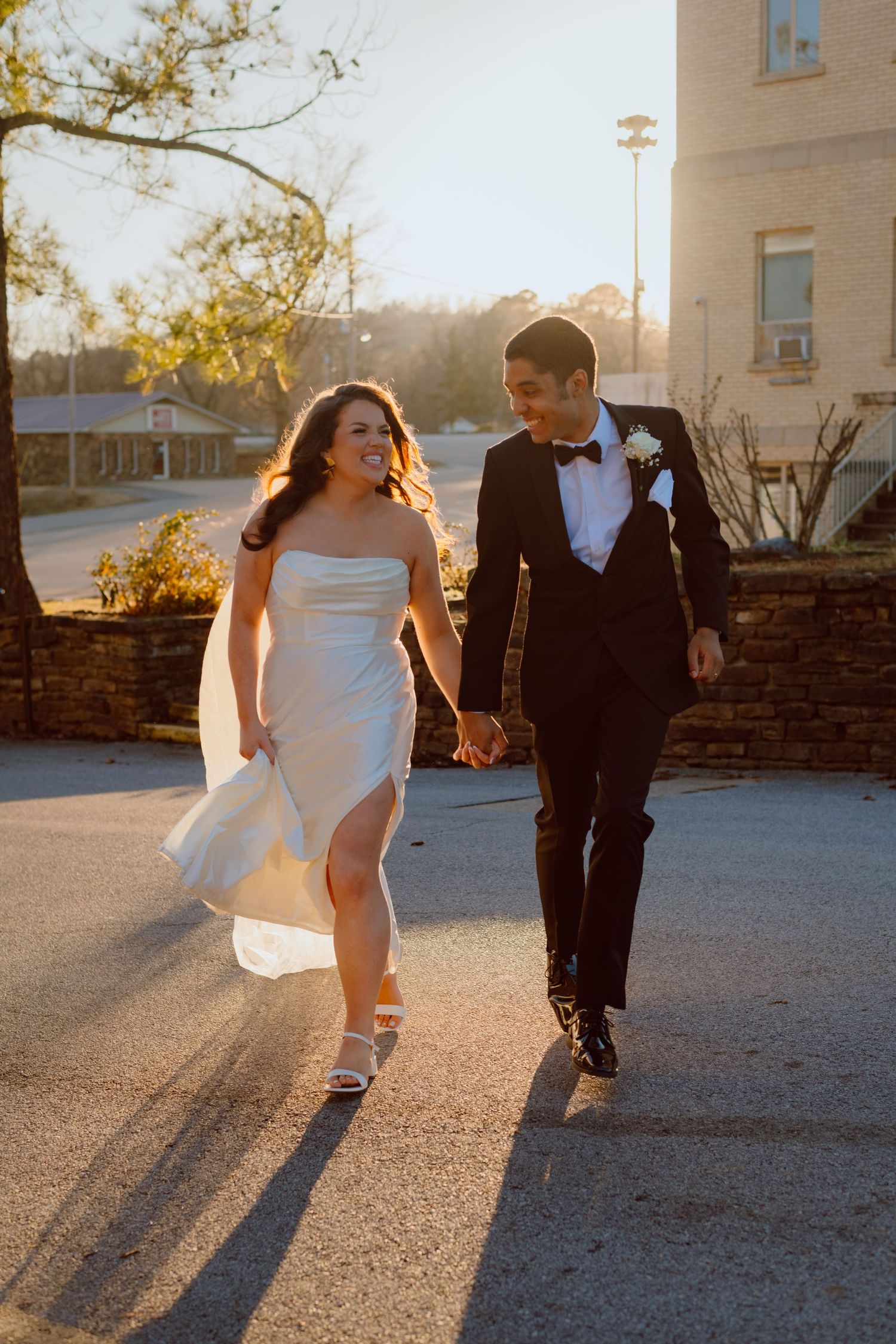 Couple in formal attire walking together during a golden sunset.