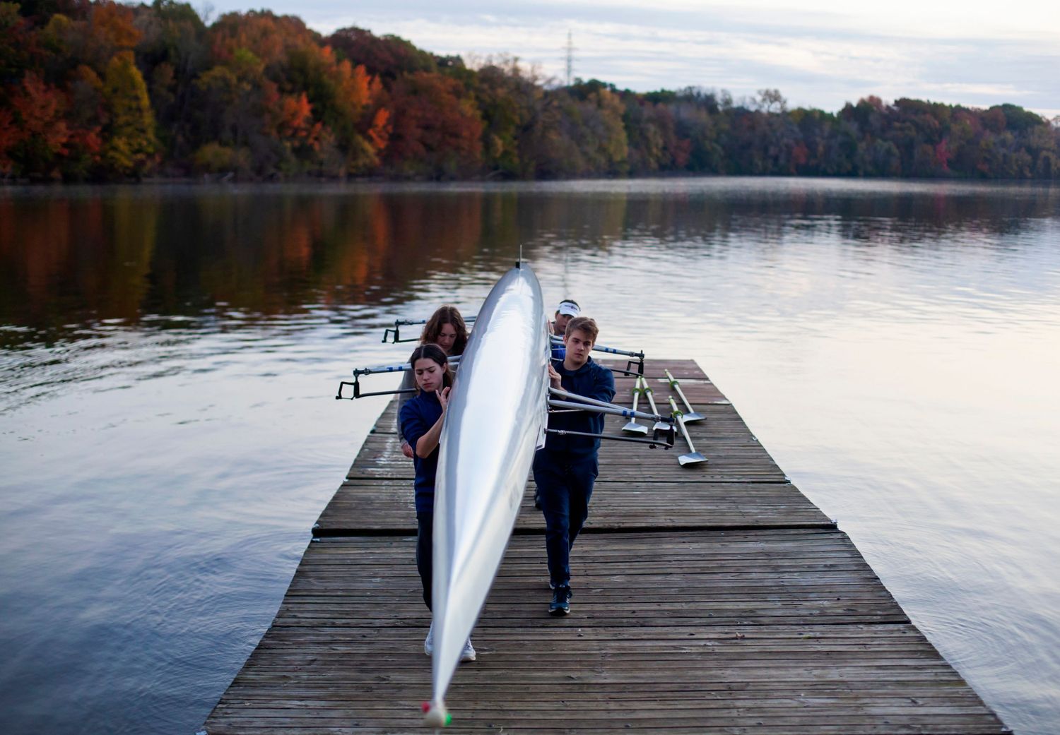 Rowers carry their boat along a dock.