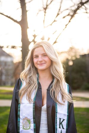 Graduate wearing black gown and decorative stole photographed at sunset.