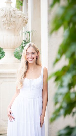 High school senior wearing white summer dress posing against columns at the Longwood Gardens fountains.