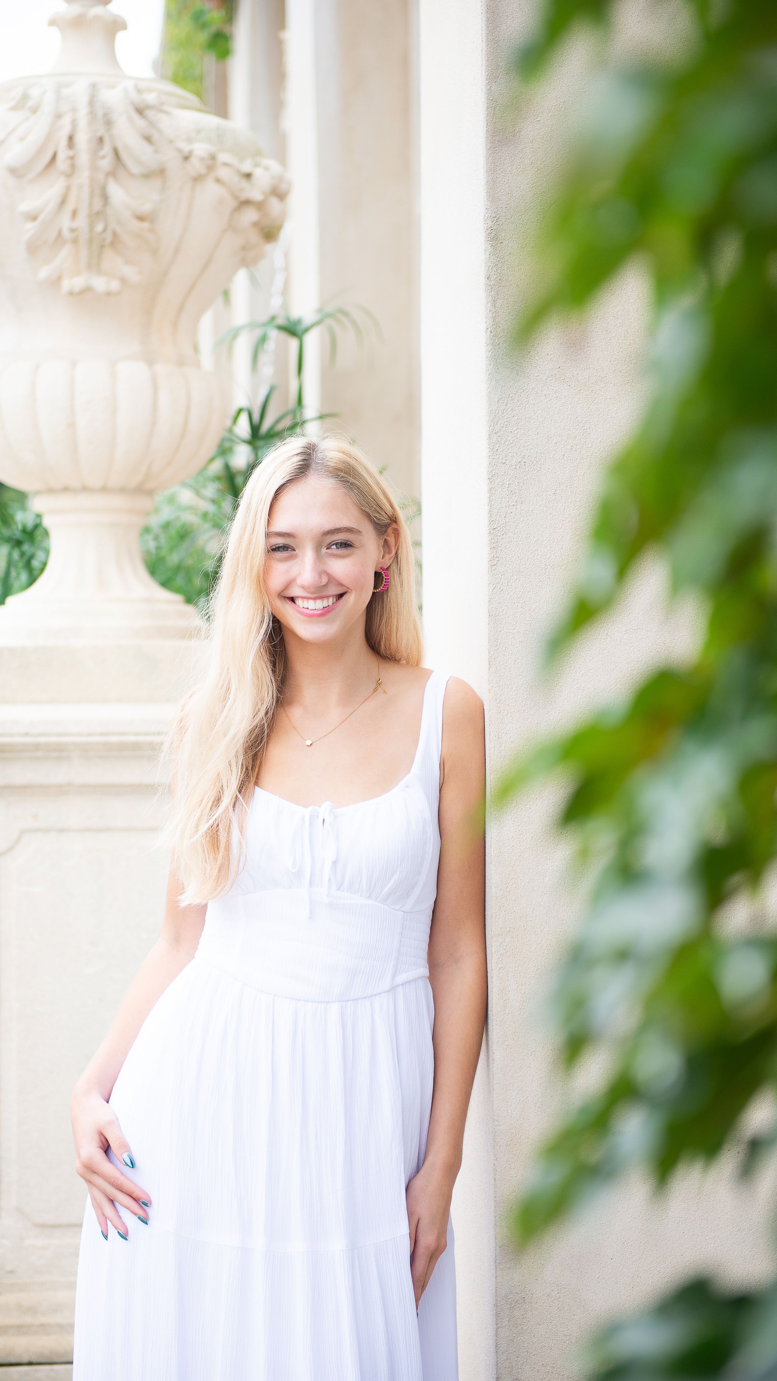 High school senior wearing white summer dress posing against columns at the Longwood Gardens fountains.