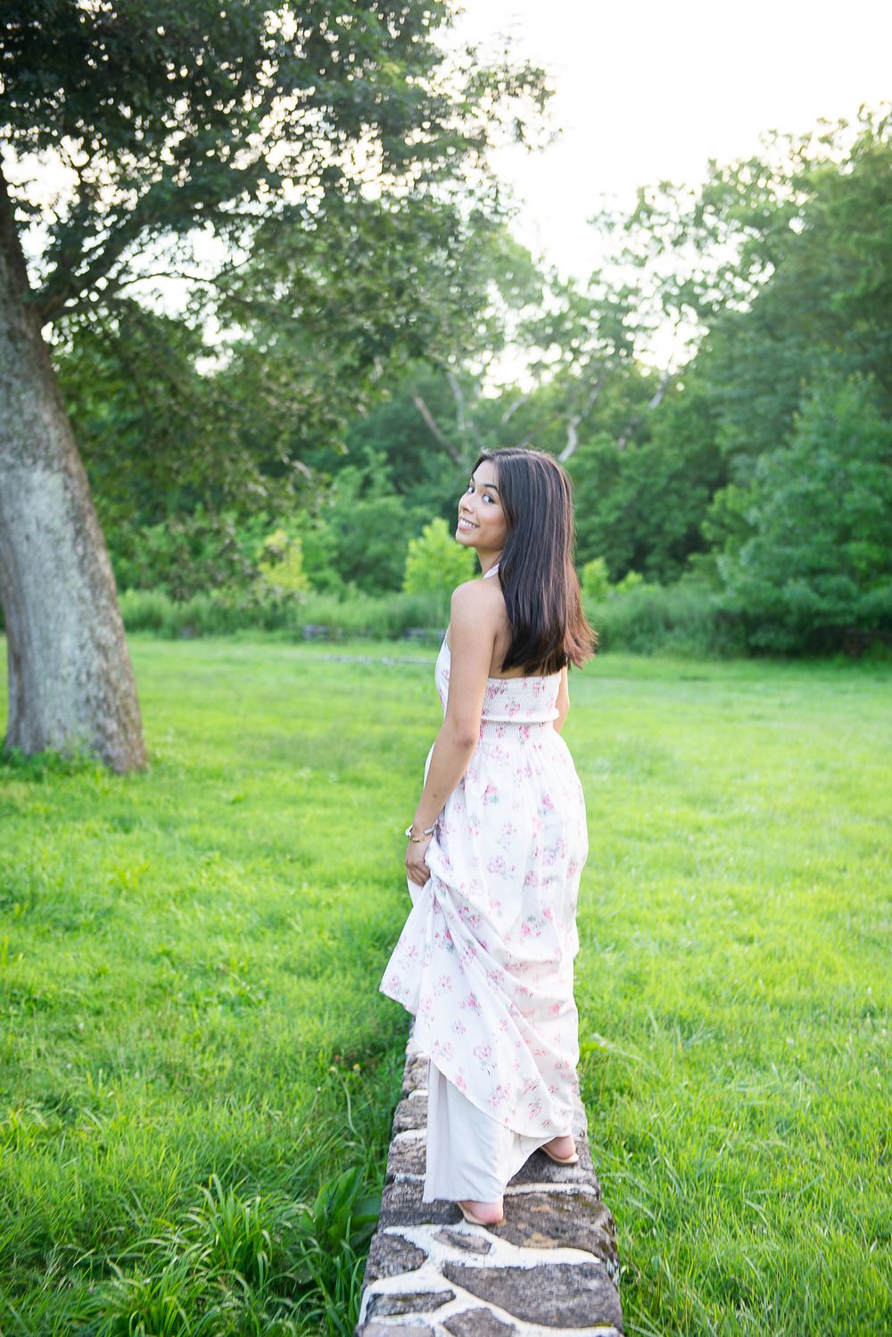 Dreamy summer portrait on stone wall surrounded by green landscape.