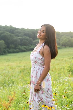 Summer portrait in floral dress standing among wildflowers in sunny meadow.