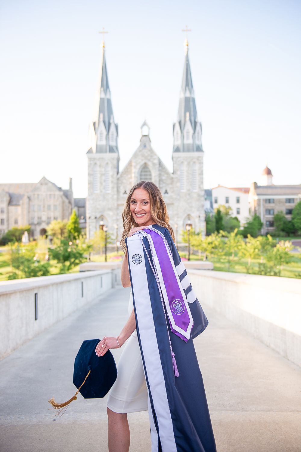 Graduate in cap and gown poses with St Thomas Church at Villanova.