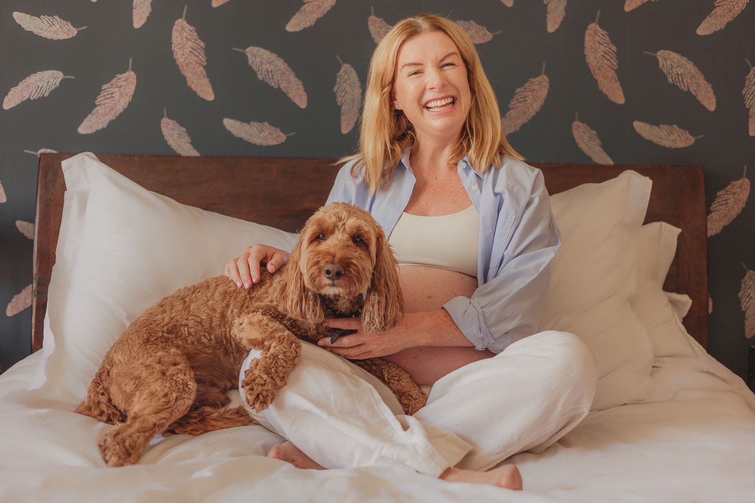 pregnancy / maternity photoshoot in Balham - pregnant mum sitting smiling on bed with cockapoo dog