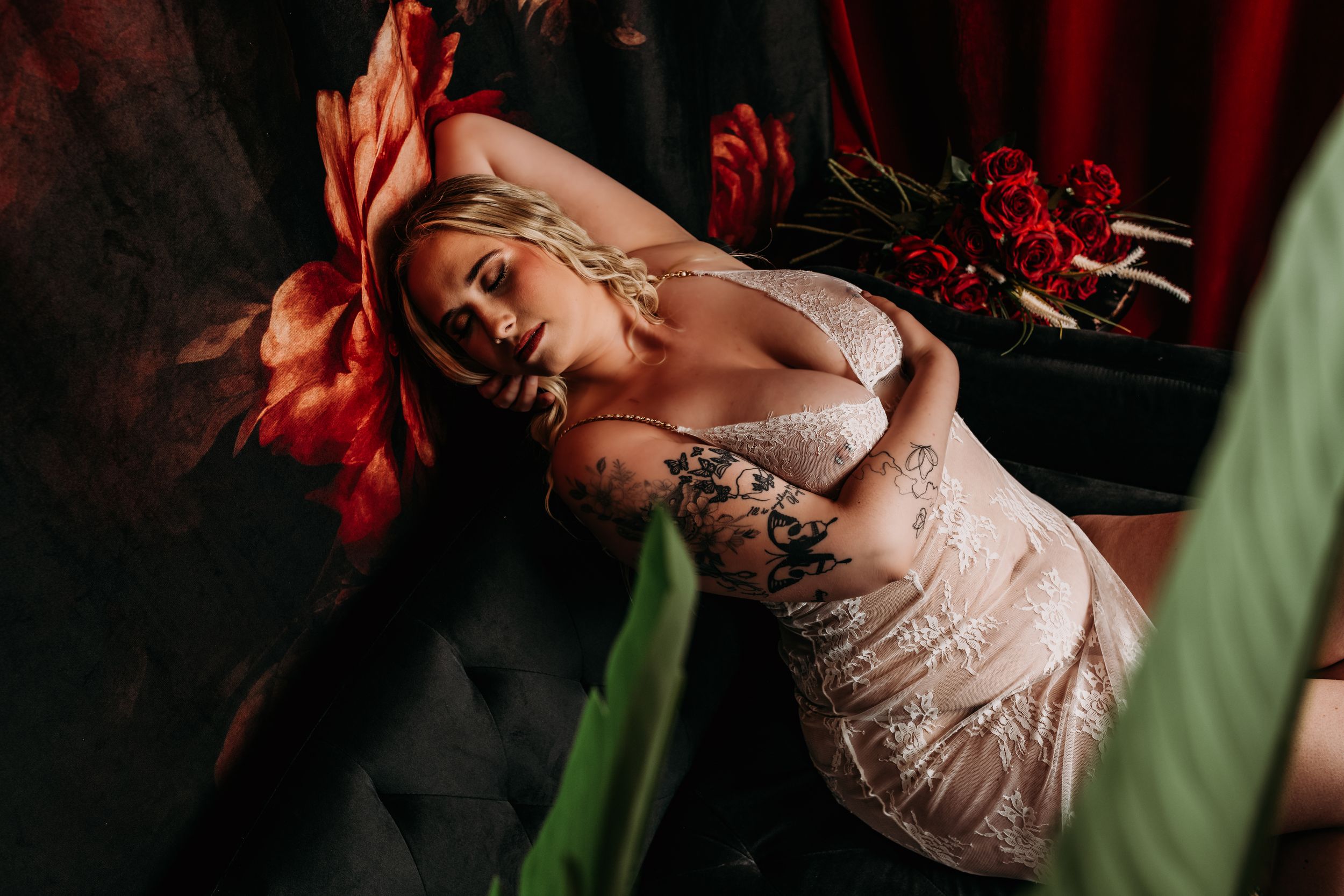 A moody artistic portrait in dramatic red lighting captures someone posing near green foliage. Boudoir Photography Studio Grand Rapids