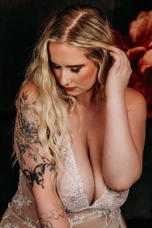 A woman in white lace lingerie with blonde hair and artistic tattoos poses in a boudoir style photo. Boudoir Photography Studio Grand Rapids