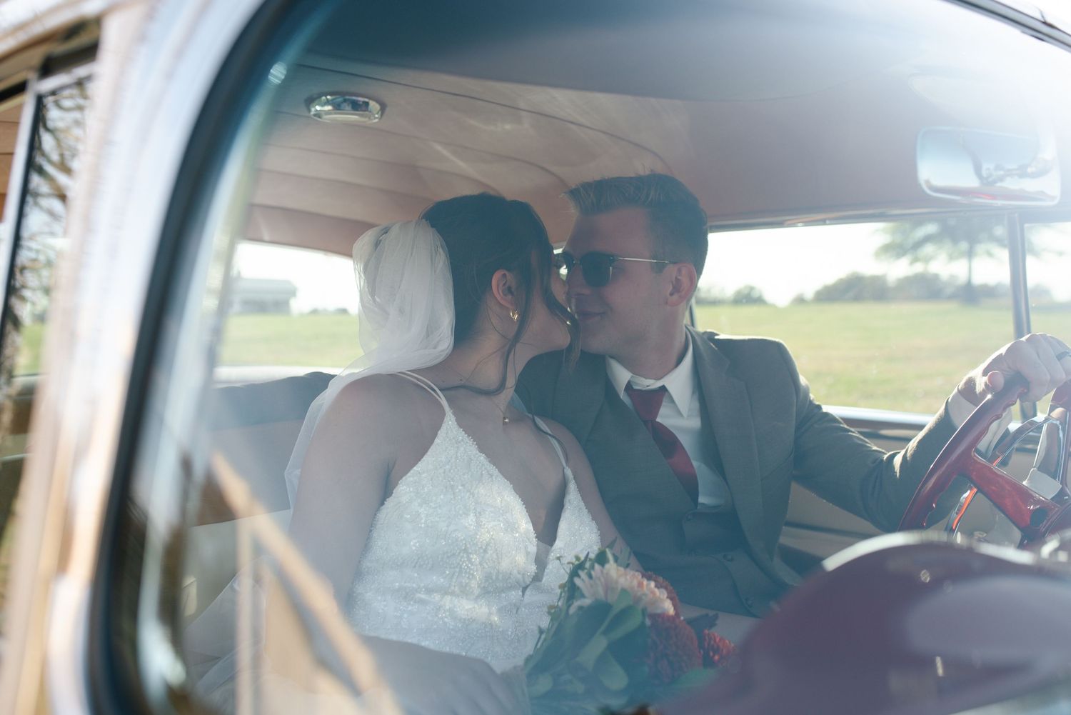 A romantic moment captured through a car window showing a couple in wedding attire sharing an intimate moment.