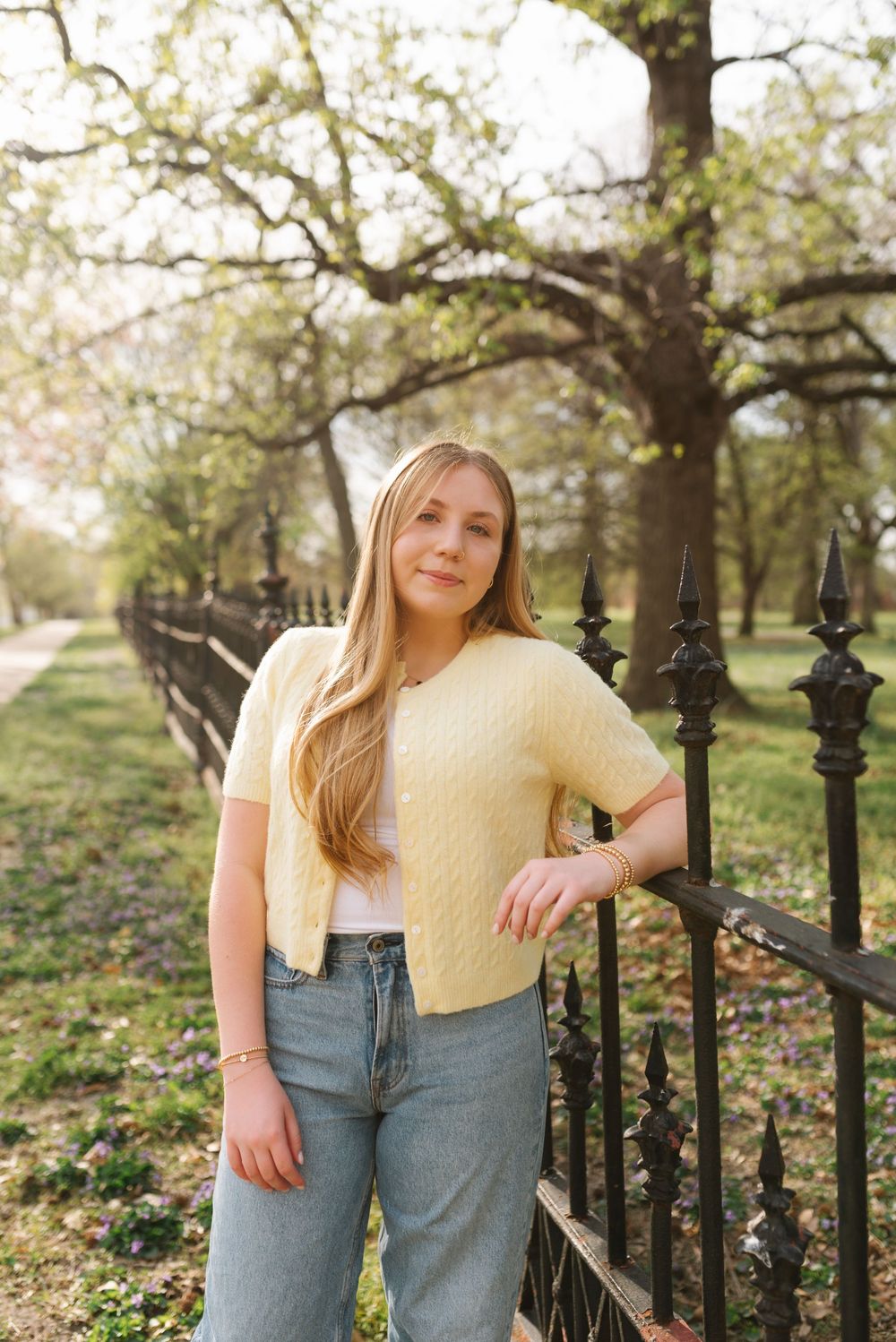 A casual spring photoshoot in front of a decorative iron fence wearing a yellow top and denim jeans.