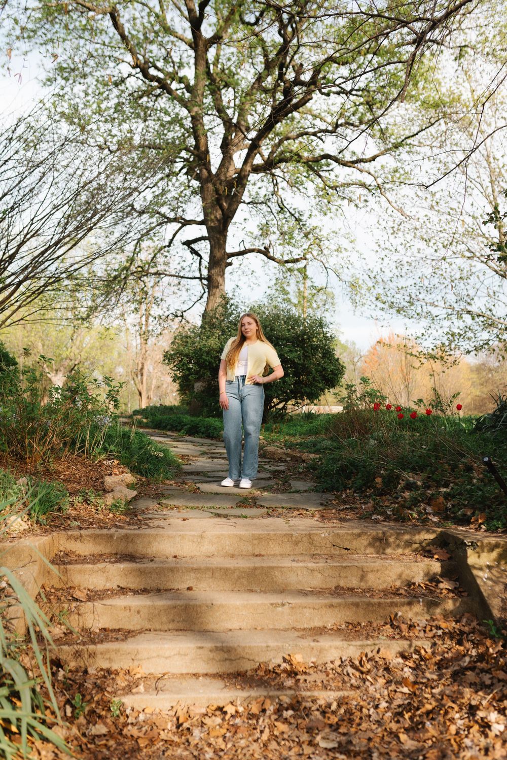 A stone path leads through autumn leaves under tall trees in a tranquil garden setting.