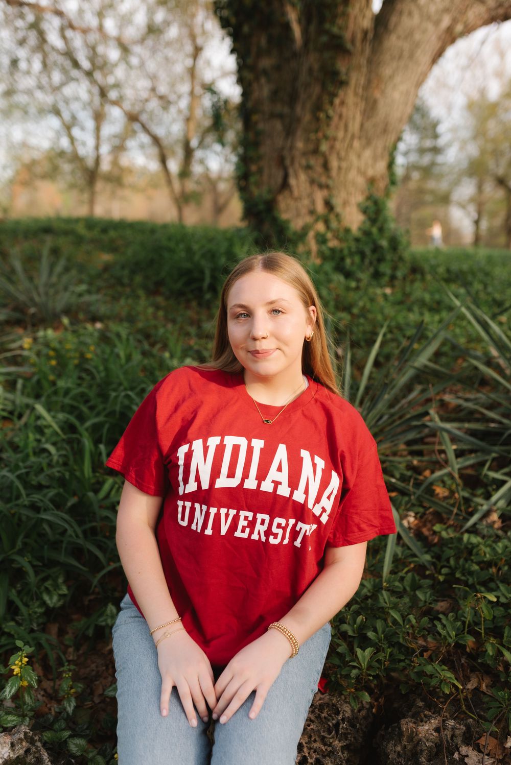 Someone wearing a red Indiana University t-shirt sits outdoors against a natural backdrop.