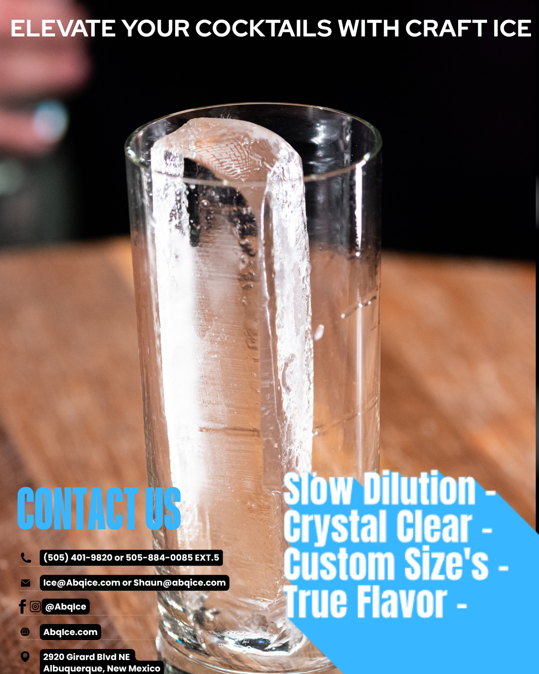 A tall clear glass containing a crystal clear ice spear and blurred background highlighting craft cocktail presentation.