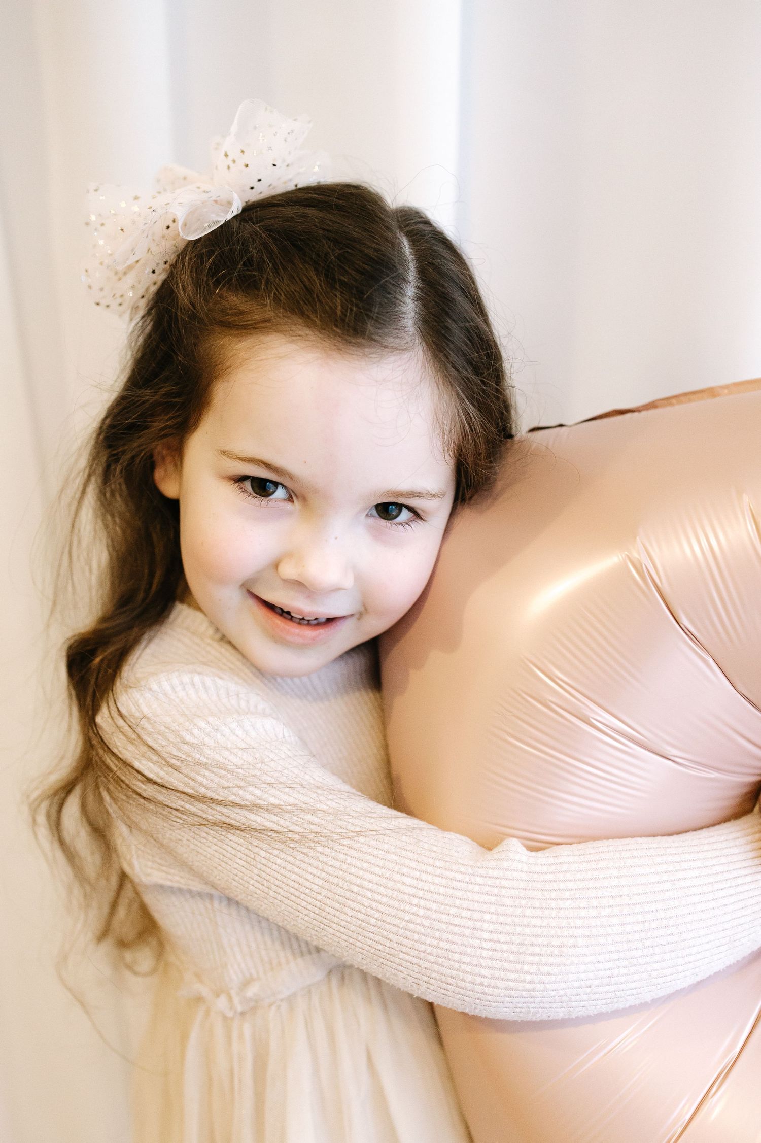 A child with dark hair in a beige sweater looking upward with lit pink and white flowers in the foreground.