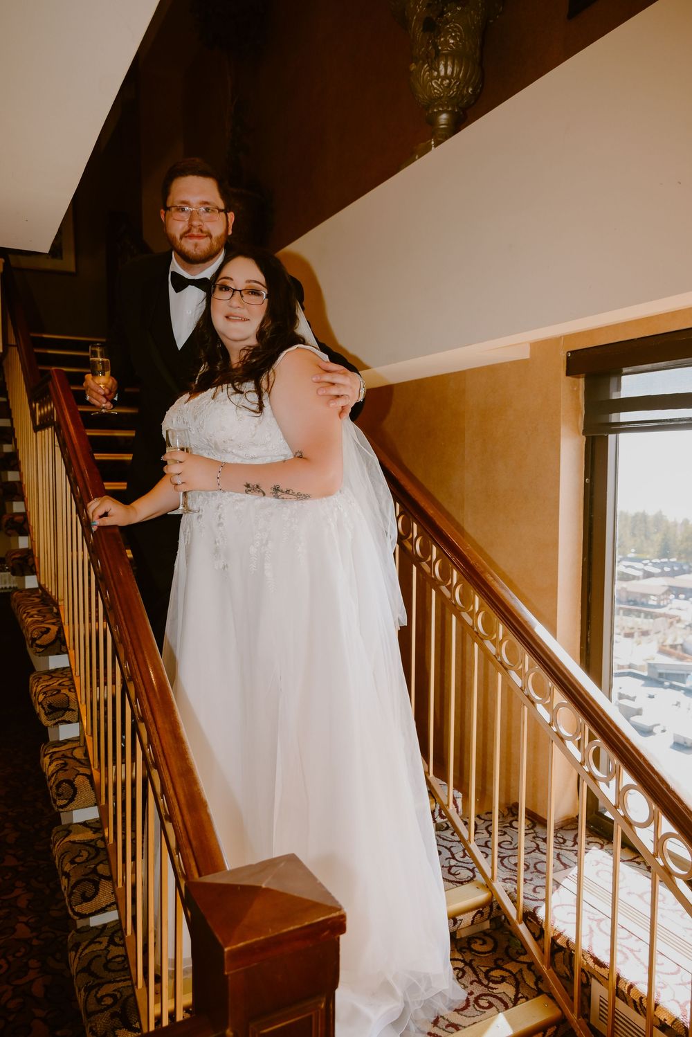 A couple stands together on ornate carpeted stairs in wedding attire, with warm lighting creating an intimate atmosphere.