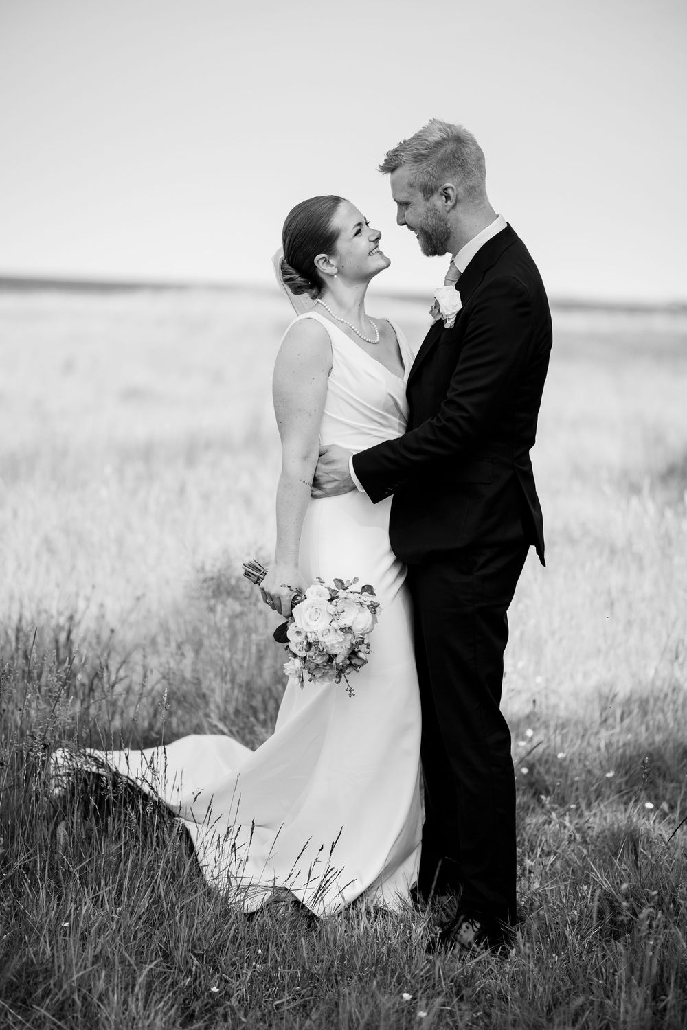 A romantic black and white wedding portrait of a couple embracing in a field.