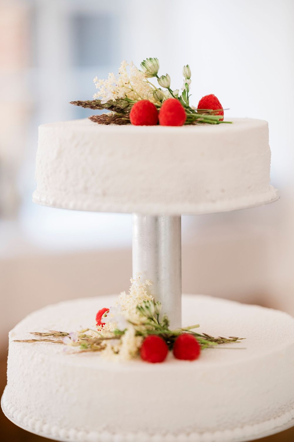 A two-tier white wedding cake decorated with fresh red berries and delicate white flowers on a pedestal stand.
