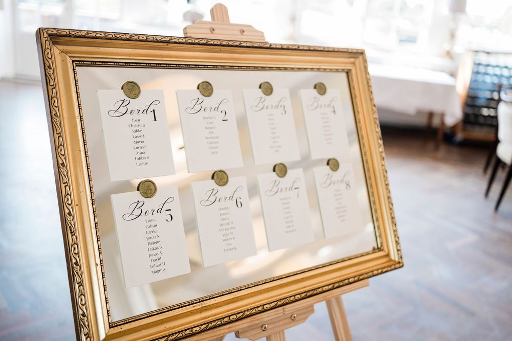 An elegant gold-framed seating chart display with multiple paper cards arranged neatly showing table assignments.