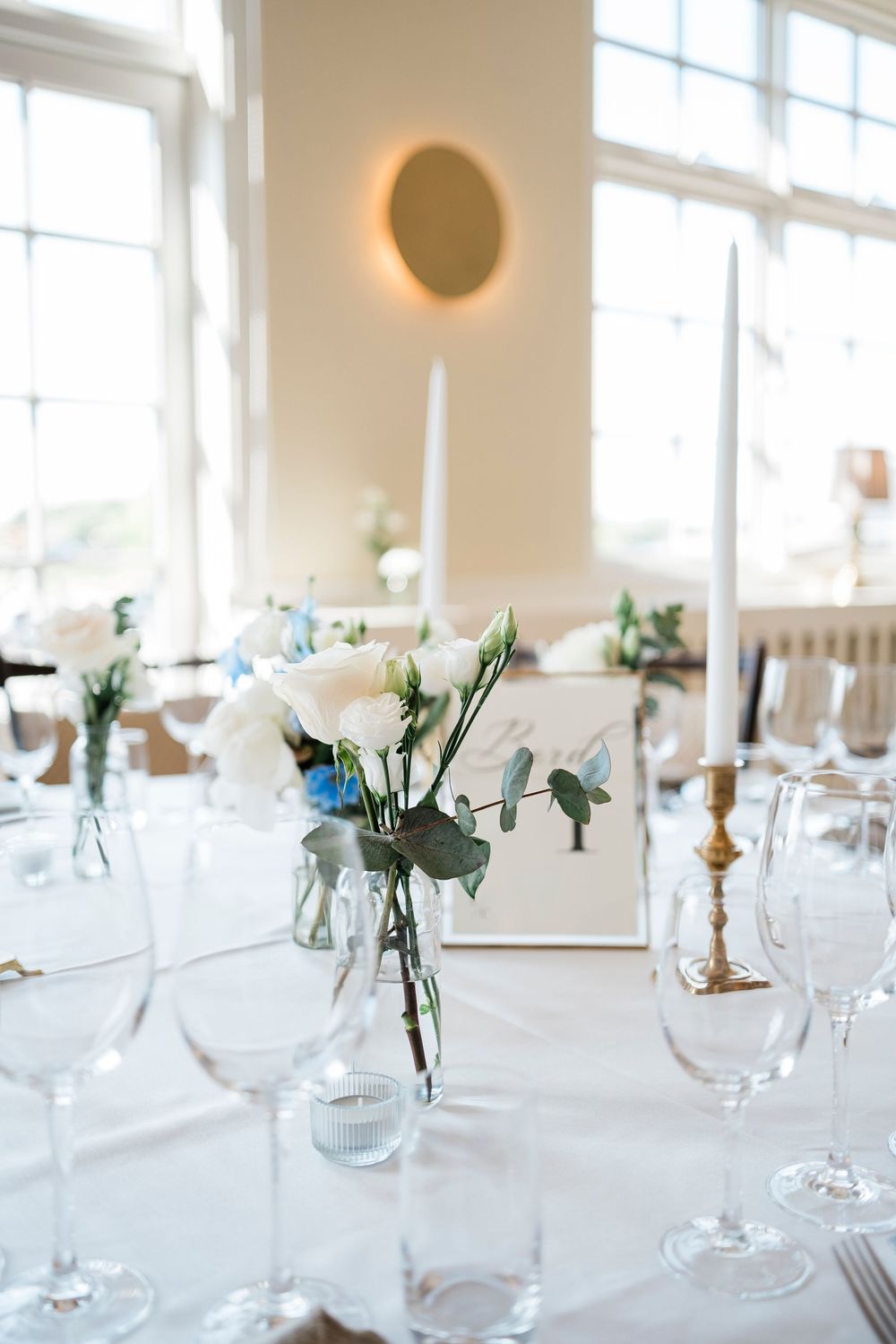 Elegant wedding reception table setting with delicate white floral centerpieces in glass vases and stemware.