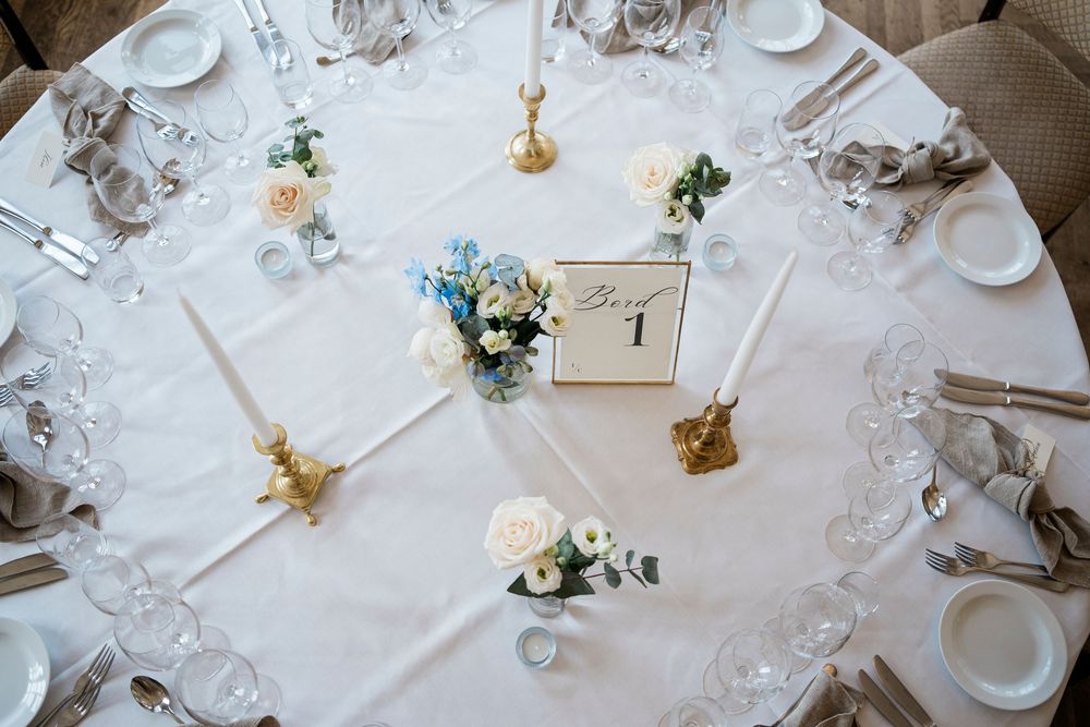 Overhead view of a formal round dining table with white linens, table number one, and floral centerpieces.