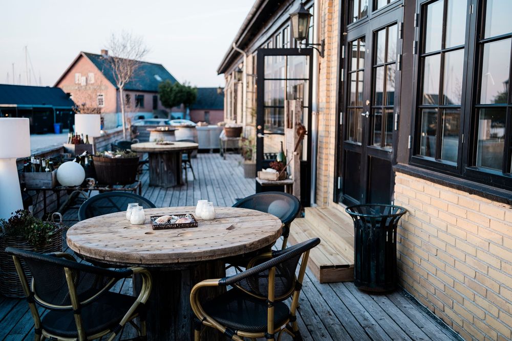 Cozy outdoor deck seating area with wooden tables and chairs overlooking a scenic mountain landscape at sunset.