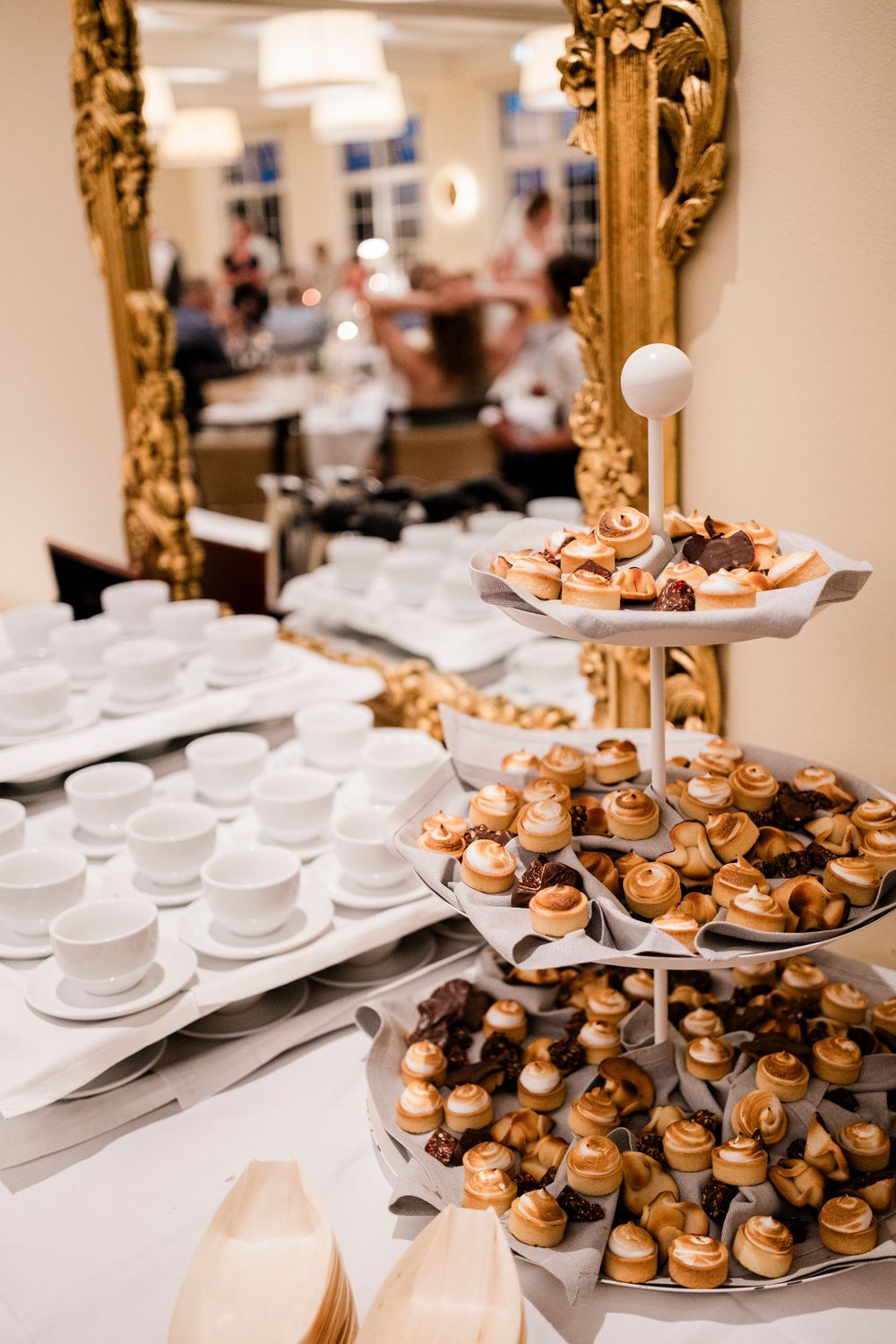 Tiered dessert display with miniature pastries and coffee cups beside an ornate gold mirror.