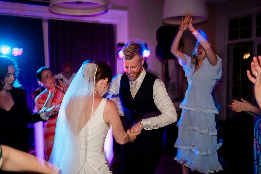 Wedding celebration with dancers enjoying themselves on a dimly lit dancefloor with purple and blue lighting effects.