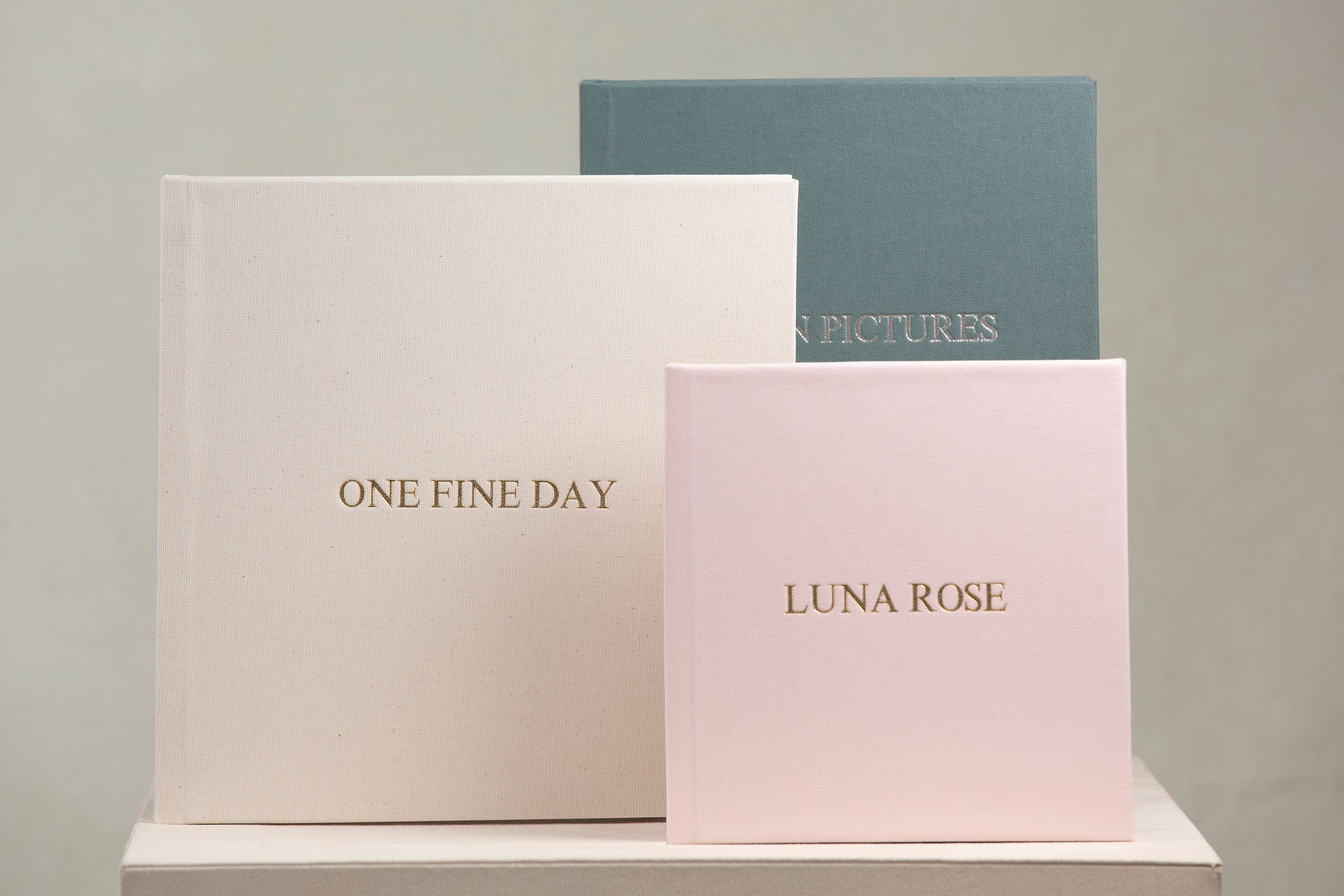 Three elegant wedding album books in white, pink, and blue arranged on a white display shelf.