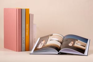 Open photo book displaying interior design layouts with soft pink hardcover books standing vertically in the background.