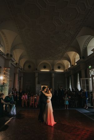 Couples dancing in an elegant ballroom with a dark ambiance and dramatic lighting beneath an arched ceiling.