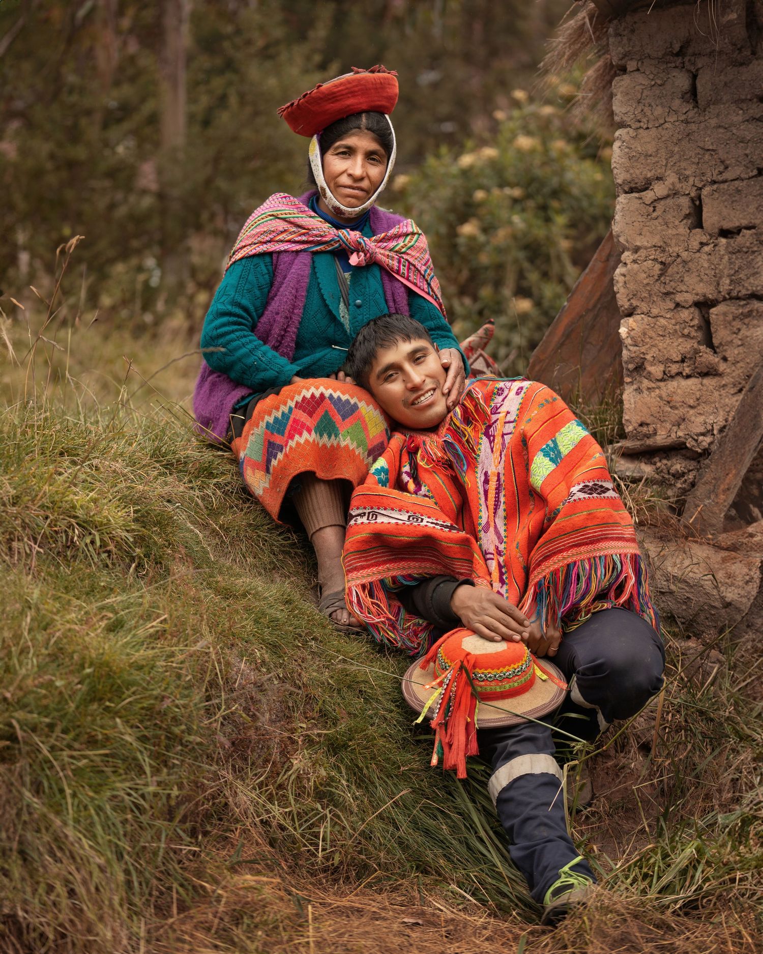 People in traditional Andean clothing resting against stone wall on hillside.