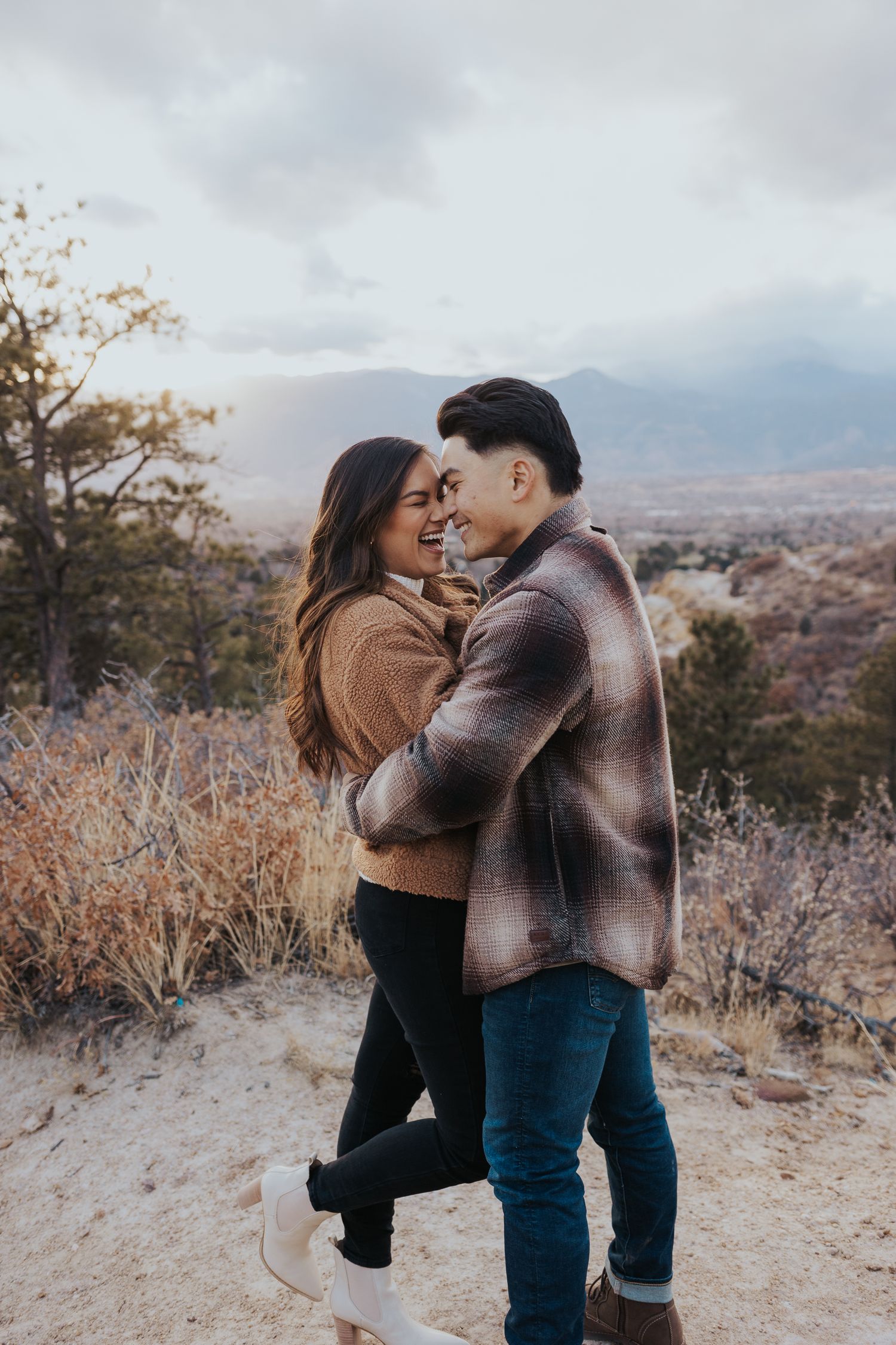 Couple embraces and laughs together on scenic hilltop overlook during autumn day.