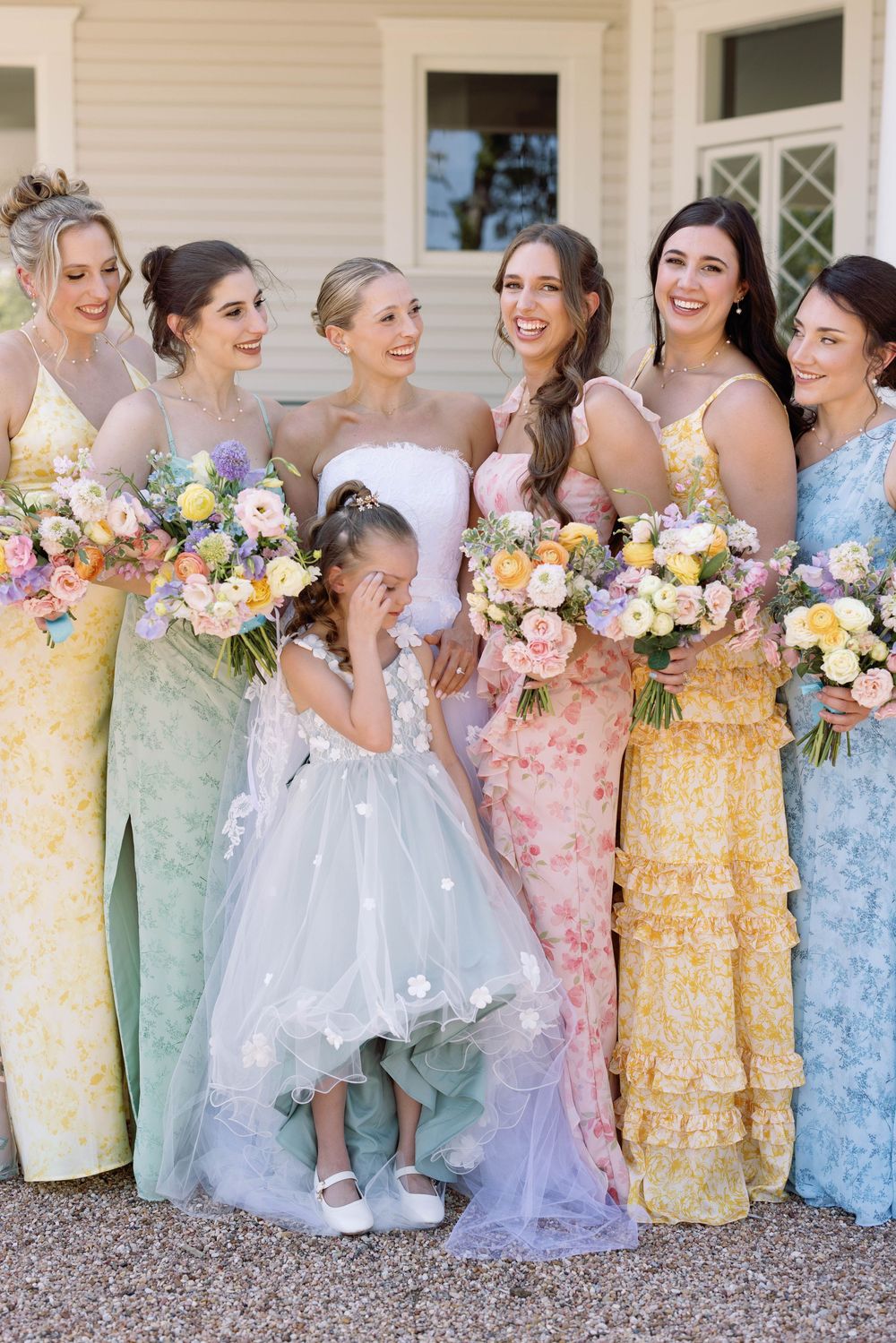 Wedding party wearing pastel-colored floral dresses holding beautiful spring bouquets of yellow and pink flowers.