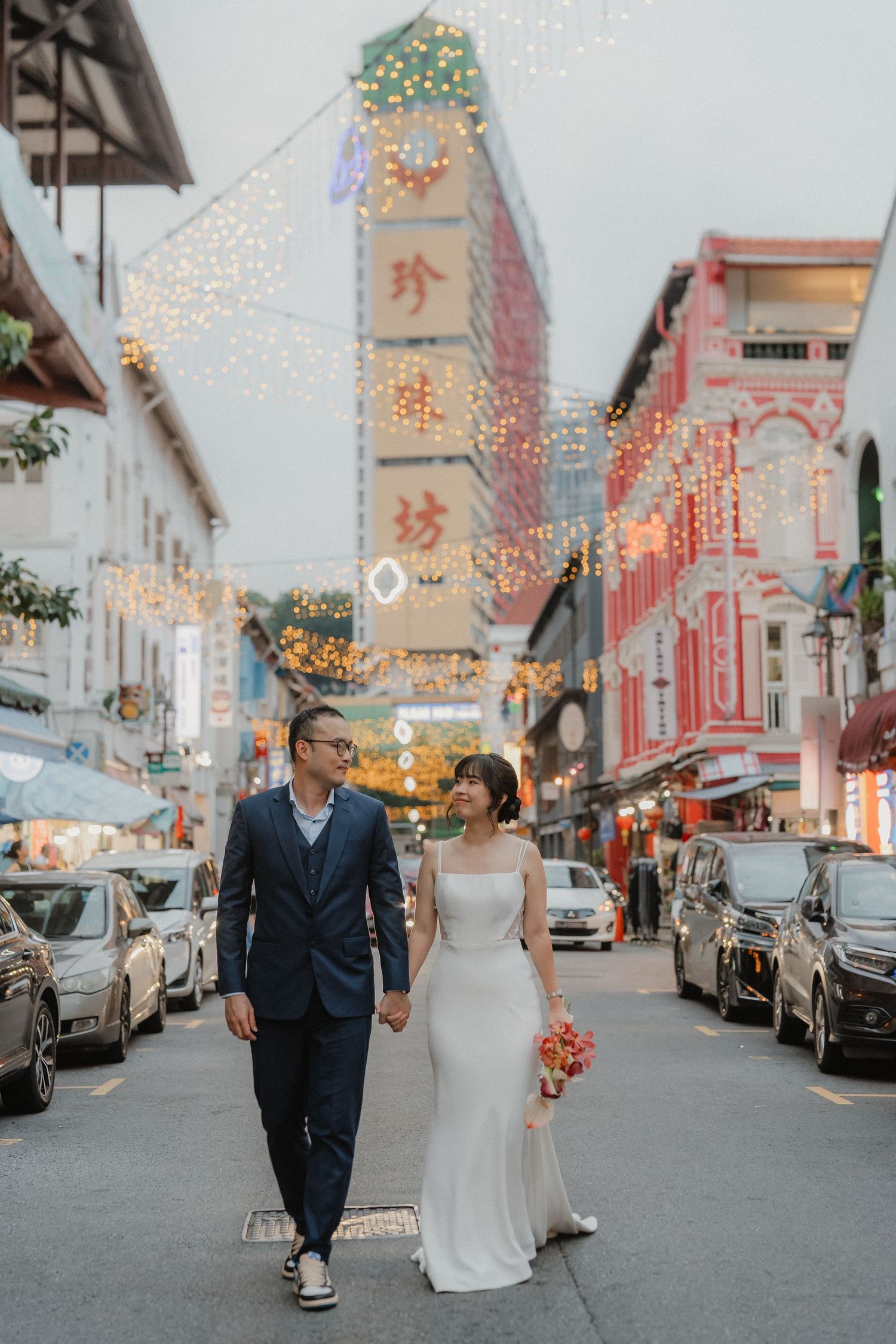 A couple walks down a festive city street lined with sparkling lights and Chinese storefronts.