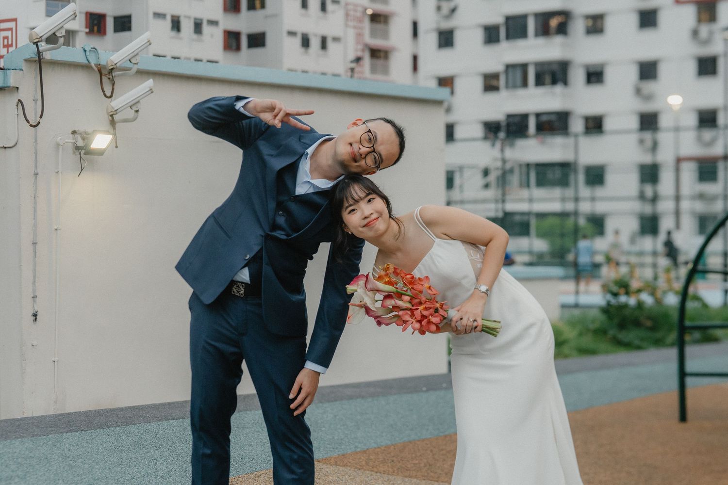 A newlywed couple poses together against an urban apartment building backdrop with modern architectural details.