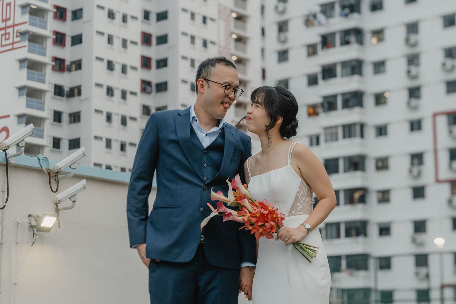 A romantic wedding couple embraces in front of apartment buildings on their special day.
