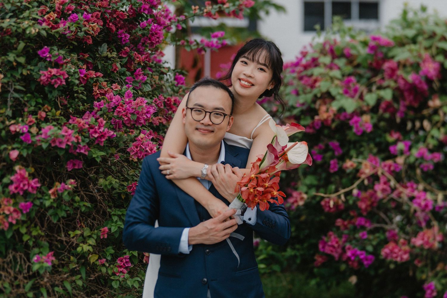 A romantic moment captured in front of blooming pink bougainvillea flowers during an outdoor wedding shoot.