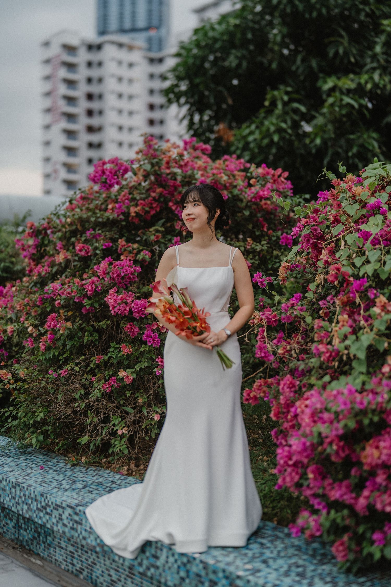 A person in a white wedding dress sits on a stone wall surrounded by blooming pink bougainvillea flowers.
