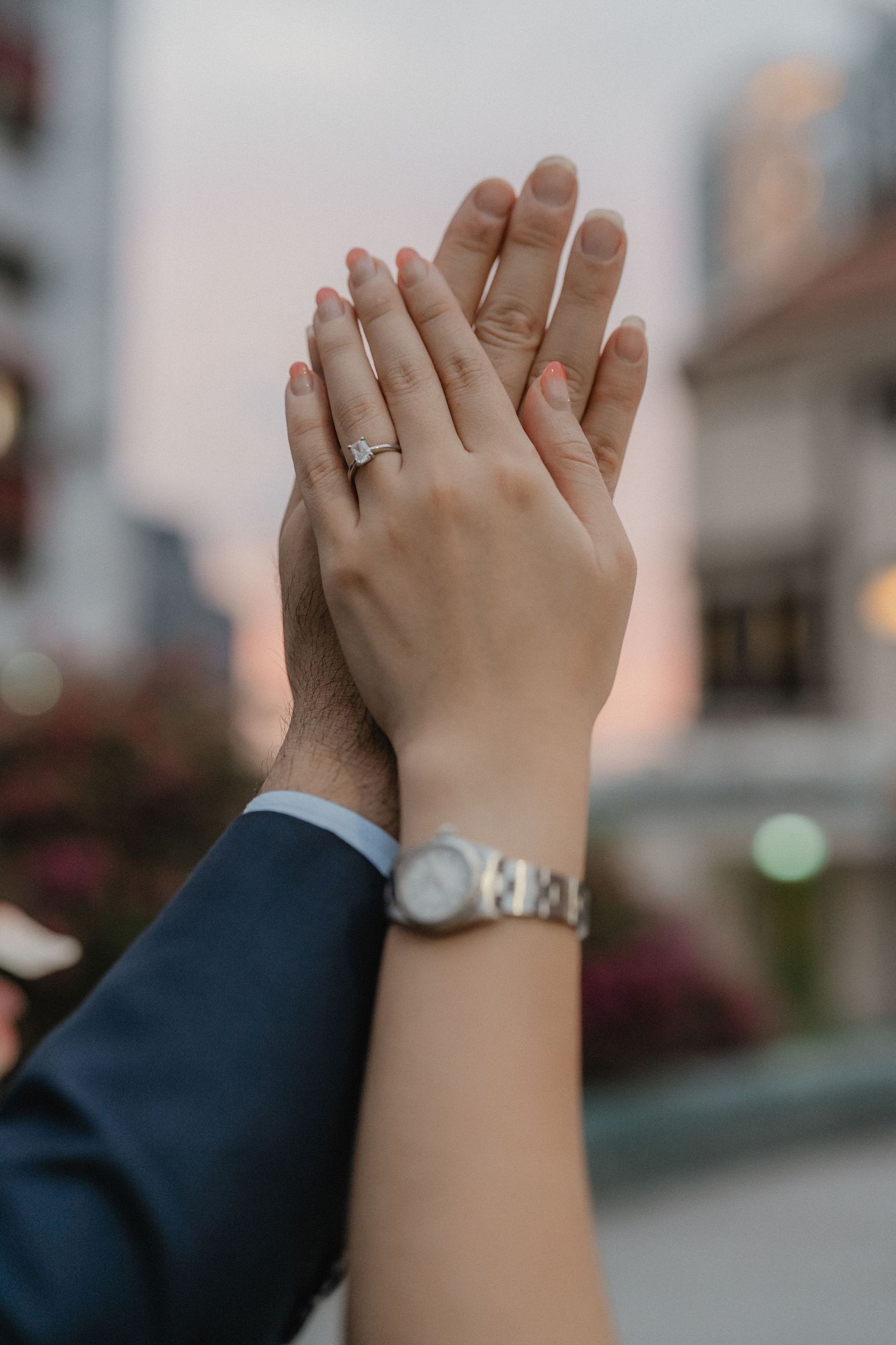 Closeup of engaged couple's hands with engagement ring, showing affection against an urban backdrop.