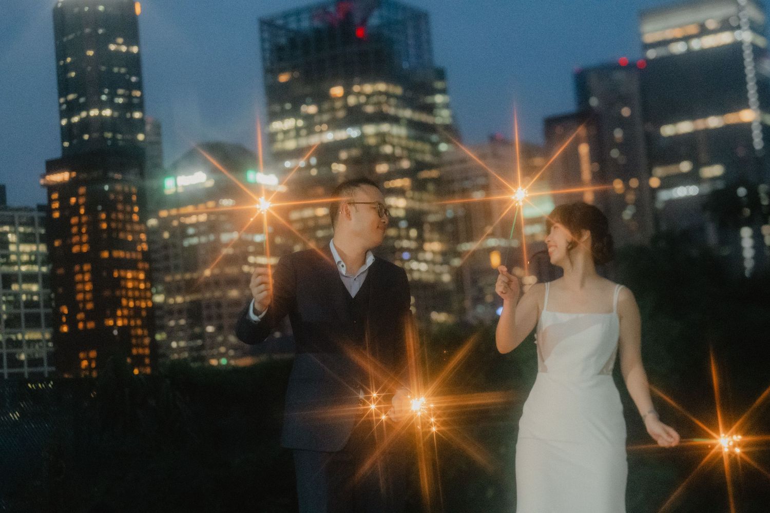 Romantic couple silhouetted against glowing city lights create a magical nighttime wedding portrait.