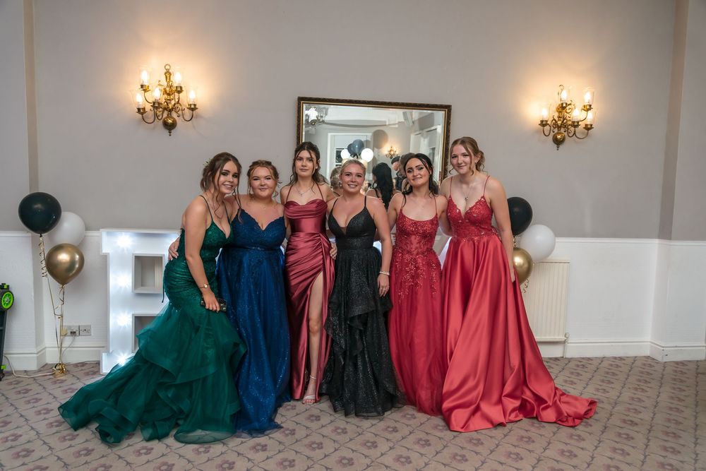 Group poses together in elegant formal dresses in emerald, navy, burgundy and red at an event venue.