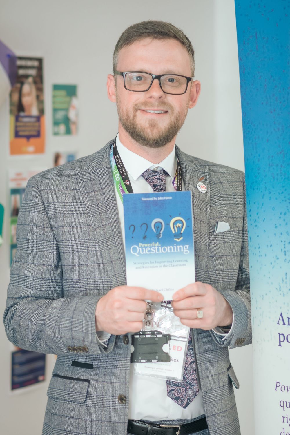 Professional in grey suit and glasses holds up a blue book about questioning while standing in an office setting.